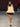 Look 02 desfile Un Romance Bien Latino 2026: vestido corto strapless de corte globo en tafetán beige y negro con rosetón en escote, zapatos de tacón con plataforma y pañuelo anudado a la cabeza.