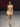 Look 05 desfile Un Romance Bien Latino 2026: top bandeau beige con rosetón central y cinta colgante con minifalda globo a tono de pretina elástica fruncida, sandalias doradas de tacón.