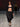 Look 09 desfile Un Romance Bien Latino 2026: blazer torero negro con top bandeau al tono y pantalón balloon oversize negro de tiro bajo con frunces en tobillos, zapatillas de tacón con pulsera y brazalete metálico.