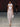 Look 15 desfile Un Romance Bien Latino 2026: vestido strapless blanco translúcido con caída amplia sobre braga a tono, gargantilla de plumas blancas y sandalias doradas de tacón.