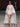 Look 16 desfile Un Romance Bien Latino 2026: túnica corta translúcida en tono blanco crudo con cuello chimenea, mangas murciélago y cola posterior sobre braga al tono, tacones beige en punta y lentes de sol burdeos.