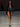 Look 22 desfile Un Romance Bien Latino 2026: blazer corto cruzado de piel negra con solapas sastre y cinto anudado al frente sobre braga a tono de tiro alto, zapatillas negras de tacón en punta y lentes de sol oscuros.